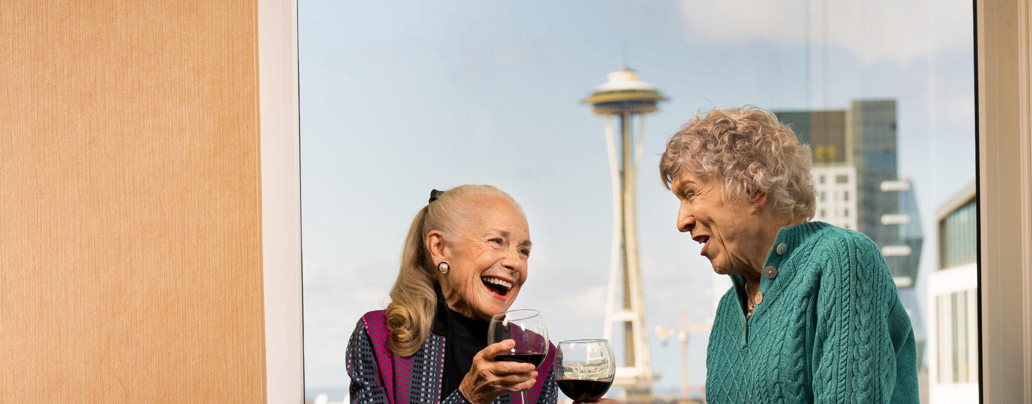 Two older women laugh and talk with glasses of wine at Mirabella Seattle.